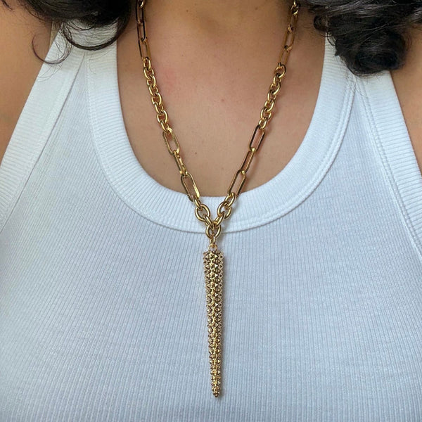Gold chain necklace with a pendant on a person wearing a white top.