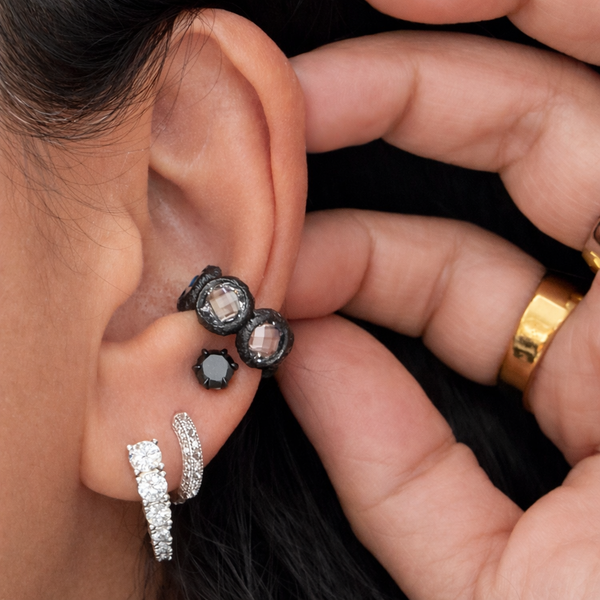 Close-up of an ear with black and silver earrings, held by a hand.