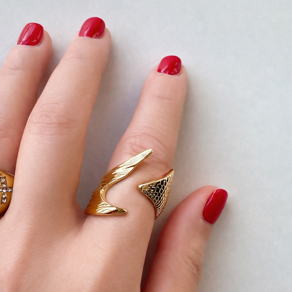 Hand wearing a gold ring with red nail polish on a light background