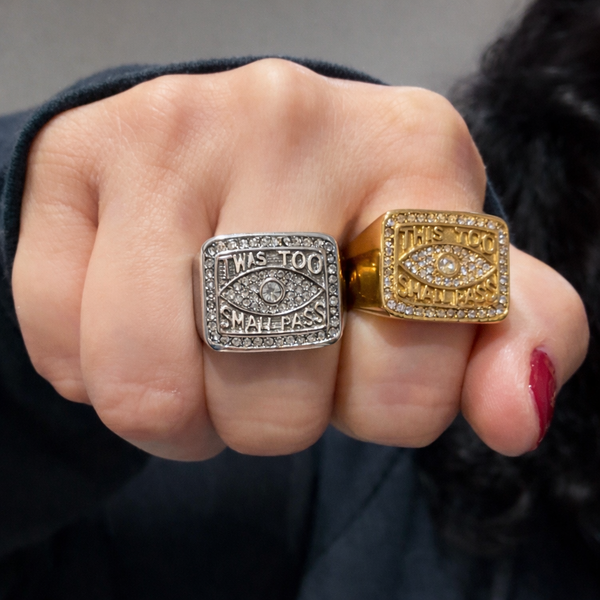 Two rings, one silver and one gold, worn on fingers against a dark background.