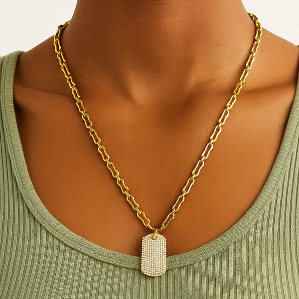 Gold chain necklace with a rectangular pendant worn by a person in a green top.