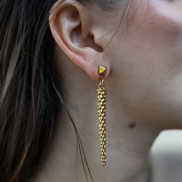 Pair of long, gold-tone studded drop earrings with a bold pyramid stud top, perfect for adding edgy elegance to any look by jagged halo jewelry.