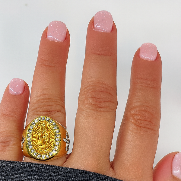 Gold ring with a religious emblem on a person's finger against a white background