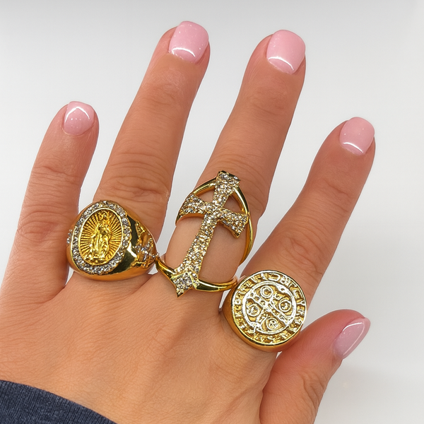 Hand wearing three gold rings with intricate designs on a light background