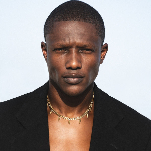 Man wearing a black jacket and gold necklace against a light blue background