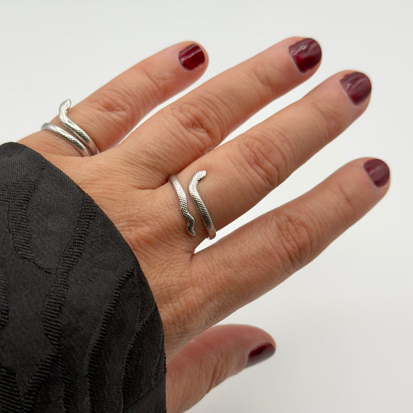 Hand wearing two silver rings on a plain background