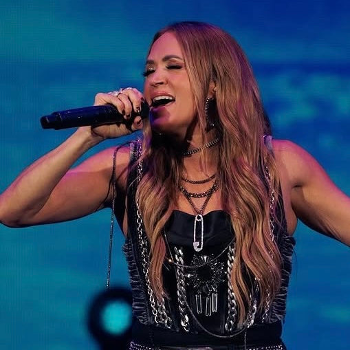 Carrie Underwood singing into a microphone with a blue gradient background
