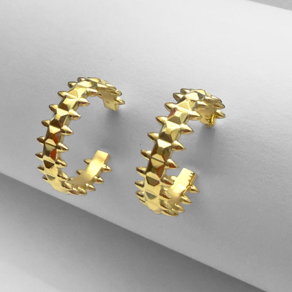 Gold hoop earrings with star-like spike design on a gray background