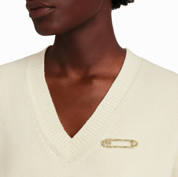 Close-up of a person wearing a cream sweater with a gold safety pin brooch.