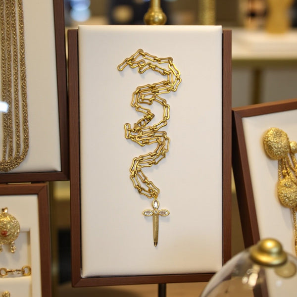 Gold necklace with a cross pendant displayed on a white card with a brown border.