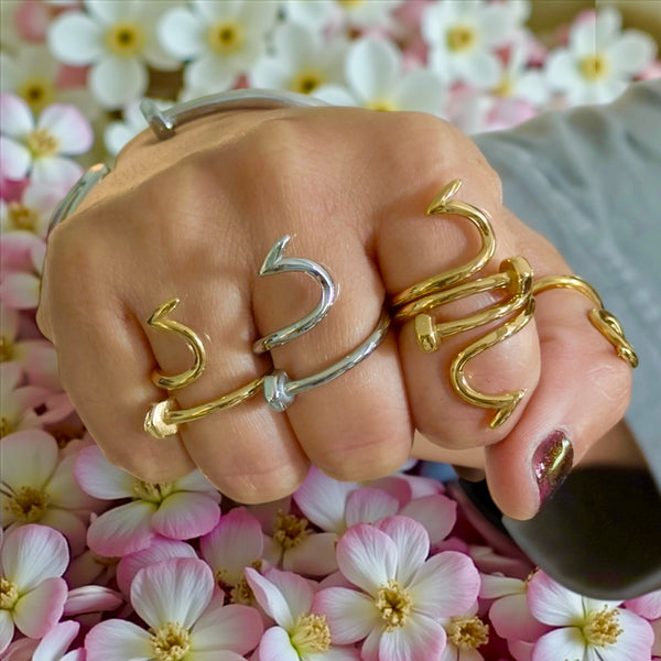 Hand wearing gold and silver nail rings nail jewelry juste clou ring on a floral background