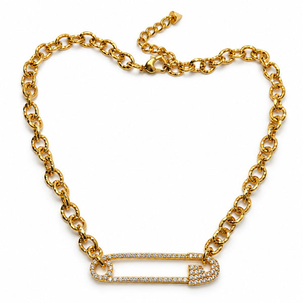 A gold chain necklace featuring a safety-pin style pendant paved with small clear stones, displayed on a clean white background.