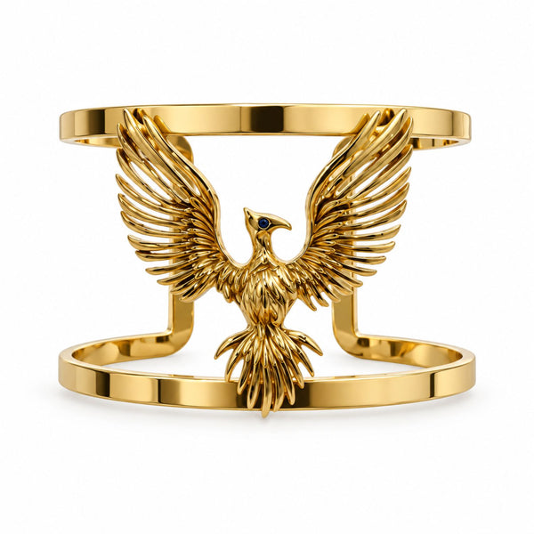 A polished gold-tone cuff bracelet featuring a highly detailed eagle with spread wings and a small dark blue eye, set against a seamless white background.