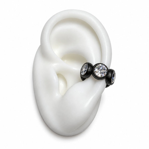 Three black ear cuff studs with clear faceted gemstones displayed on a white silicone ear model against a white background.