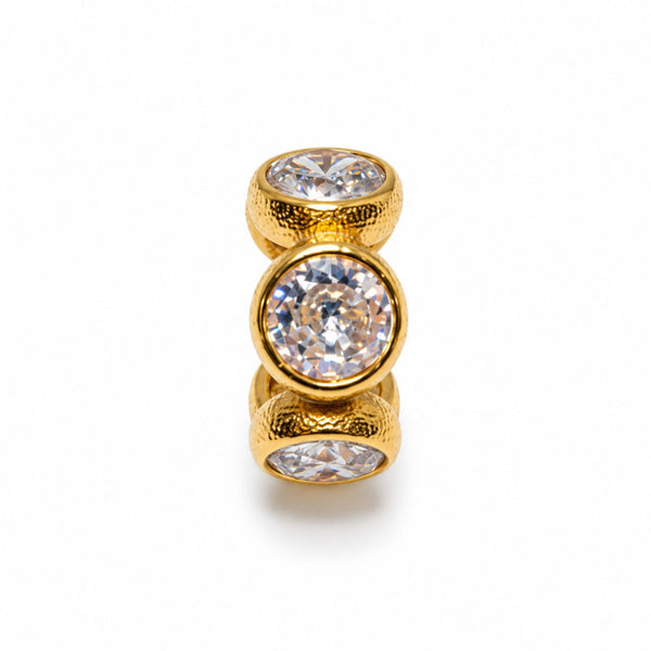 A gold ring featuring three stacked bezel-set round clear gemstones, with the center stone larger and the top and bottom stones smaller, set against a plain white background.