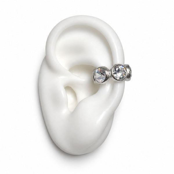 A pair of silver-toned ear cuff studs with clear faceted gemstones, displayed on a white silicone ear model against a plain white background.