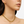 Close-up of a person wearing a gold chain necklace and matching earrings on a white background