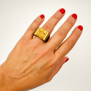 Hand wearing a gold ring with red nail polish on a plain background