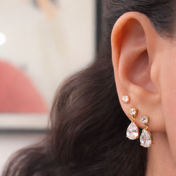 Close-up of a person wearing gold teardrop earrings with a blurred background