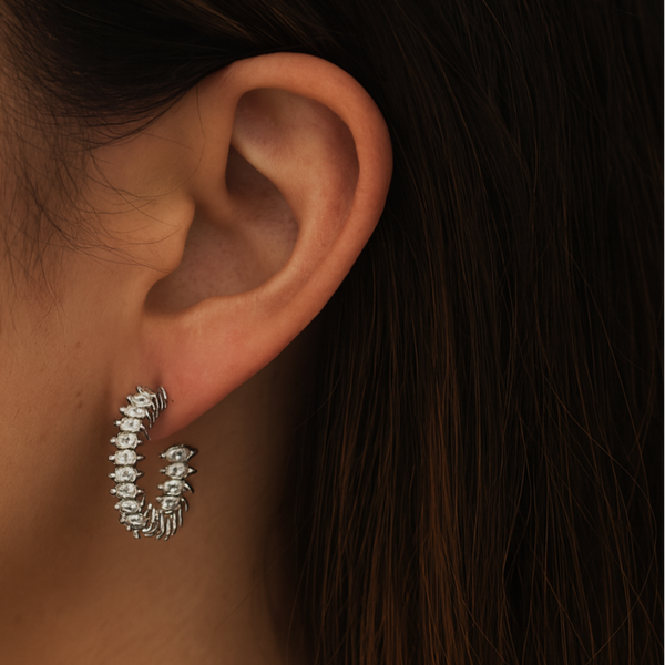 Close-up of an ear wearing a silver hoop earring with dark hair in the background