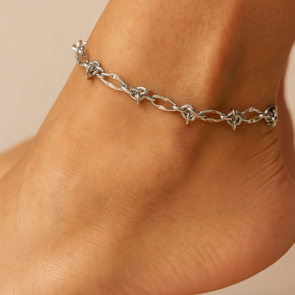 Silver anklet on a person's ankle against a beige background