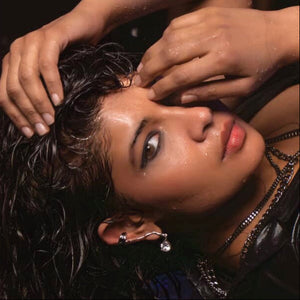Woman with wet hair and hands on her head, wearing a black top with lace details.