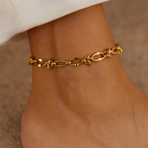 Gold chain bracelet on a wrist with a neutral background