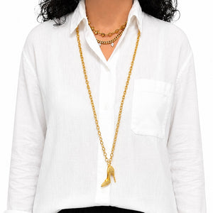 A person wearing a long gold-tone high-heeled necklace over a white button-up shirt, with a shorter gold chain layered at the neck.