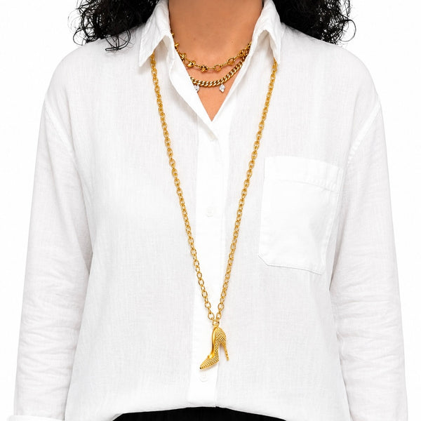 A person wearing a long gold-tone high-heeled necklace over a white button-up shirt, with a shorter gold chain layered at the neck.