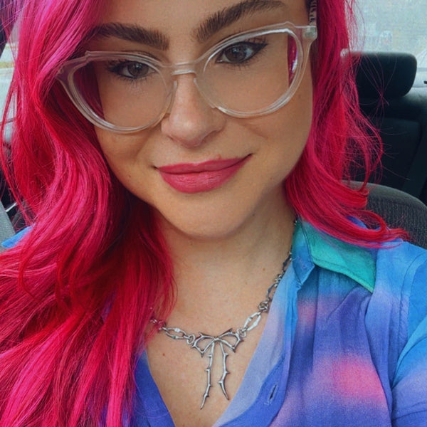 Person with vibrant pink hair and colorful shirt inside a vehicle wearing jagged halo jewelry carrie bow necklace 