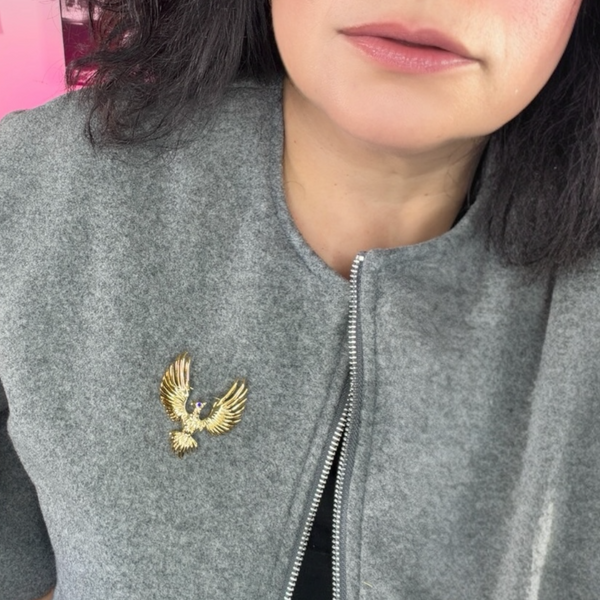 Gray jacket with a gold phoenix brooch worn by a person