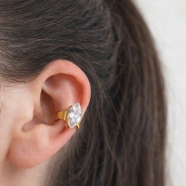 Close-up of an ear wearing a gold earring with a clear gemstone.