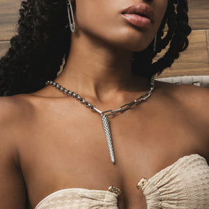Woman wearing a silver chain necklace with a textured pendant, set against a neutral background.