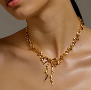Gold necklace with a bow pendant on a mannequin by jagged halo jewelry 
