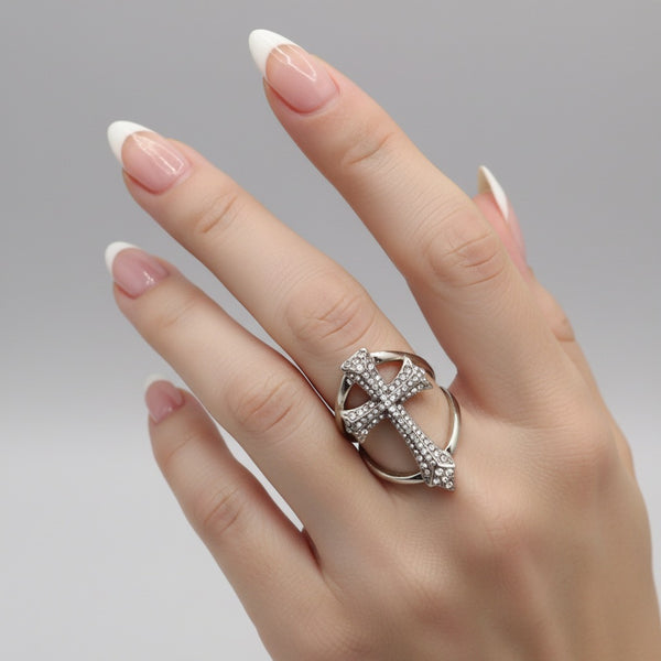 Silver ring with a cross design on a hand against a gray background by jagged halo jewelry