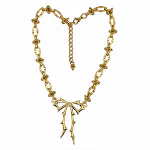 Gold chain necklace with a bow-shaped pendant on a white background.Carrie Bow Brooch in yellow gold with stainless-steel base and gold-filled bow design by Jagged Halo Jewelry.