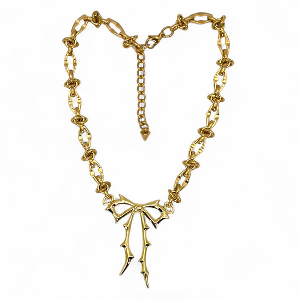 Gold chain necklace with a bow-shaped pendant on a white background.Carrie Bow Brooch in yellow gold with stainless-steel base and gold-filled bow design by Jagged Halo Jewelry.