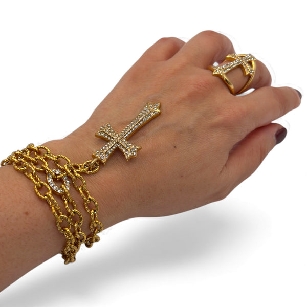 Hand wearing gold jewelry including a bracelet, ring, and cross-shaped earring on a white background saints cross necklace and ring in yellow gold by jagged halo jewelry