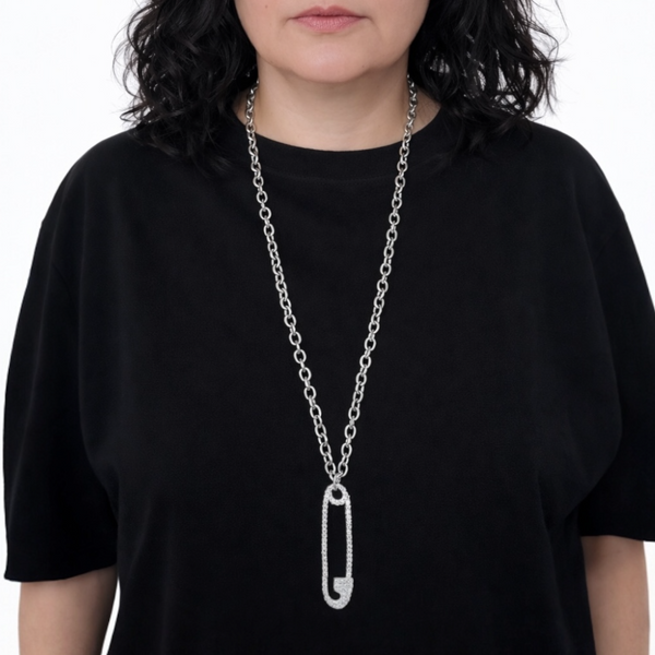 Person wearing a long silver chain necklace with a safety pin pendant on a black shirt.