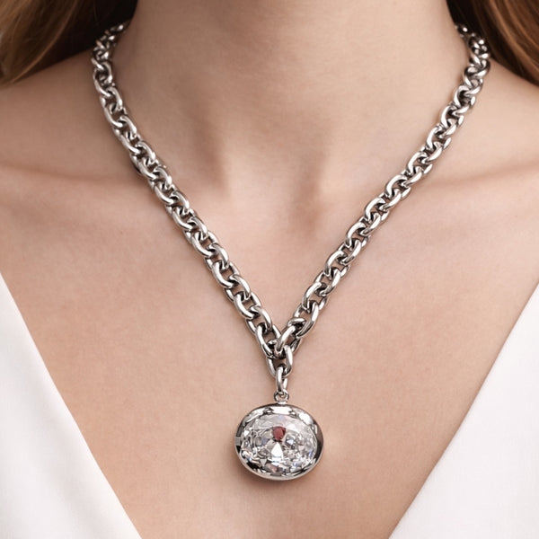 Silver chain necklace with a round pendant on a person wearing a white top.