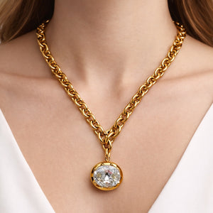 Gold chain necklace with a diamond pendant on a person wearing a white top.