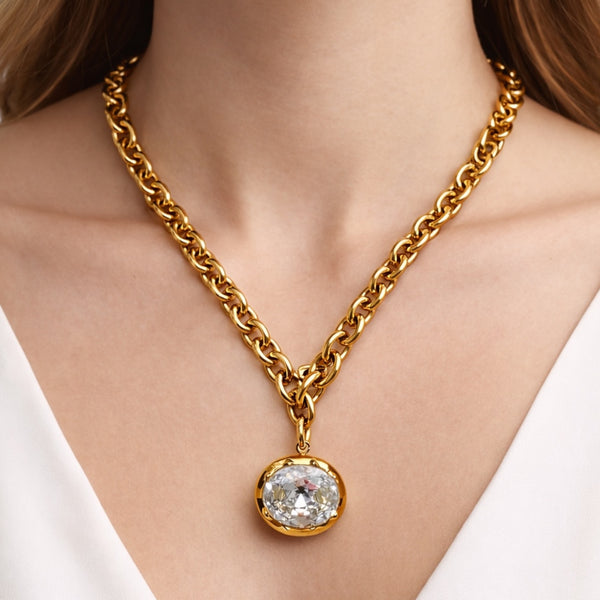 Gold chain necklace with a diamond pendant on a person wearing a white top.