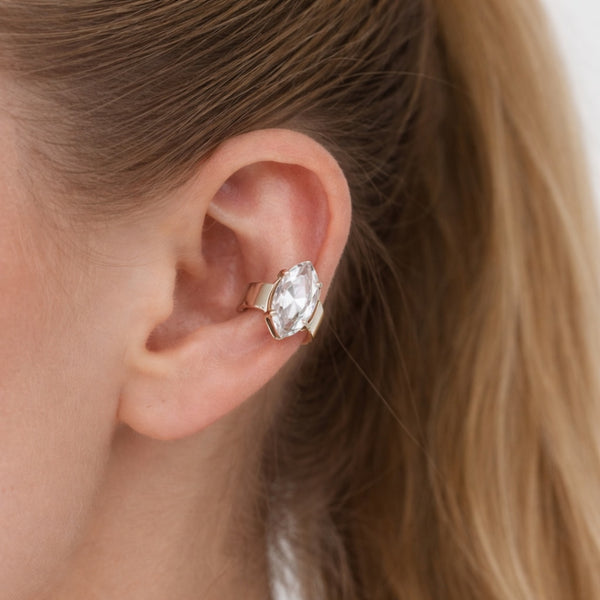 Close-up of an ear wearing a gold earring with a clear gemstone.