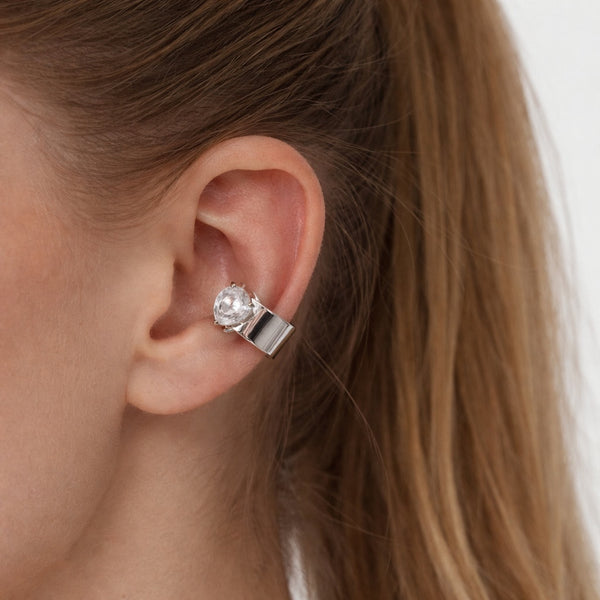 Close-up of an ear wearing a silver earring with a clear gemstone.