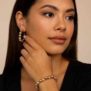 Woman wearing gold earrings and bracelet against a beige background