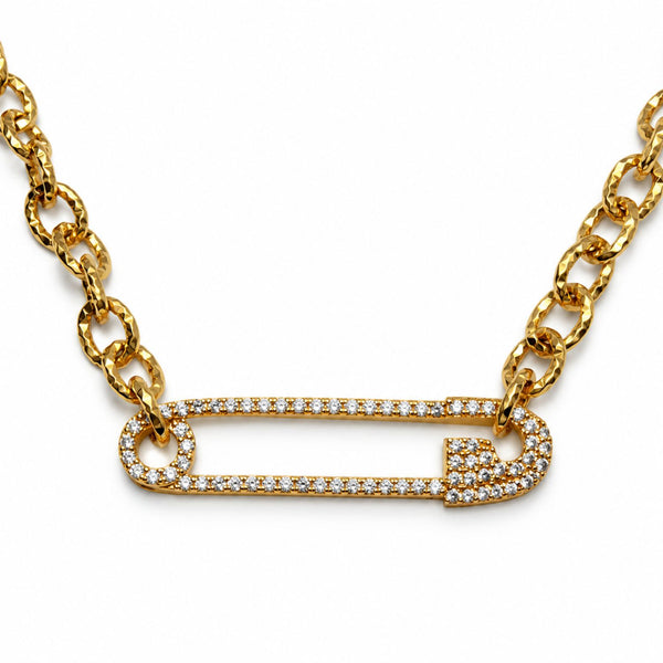 A gold chain necklace featuring a safety pin charm paved with small clear stones, shown against a plain white background.