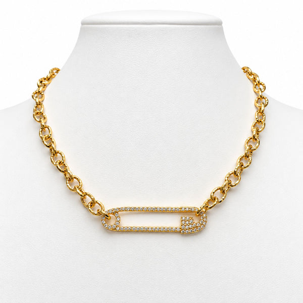 A gold chain necklace displayed on a white mannequin bust, featuring a safety-pin style centerpiece paved with small clear stones.