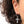 A close-up of a person's ear wearing a silver hoop earring with a dangling cross charm encrusted with small clear stones, against a white background.