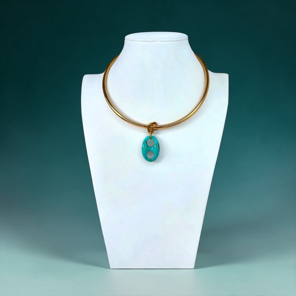 Gold necklace with a turquoise pendant on a white stand against a teal background