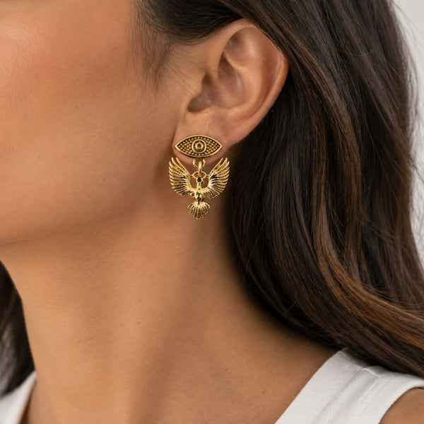 Gold phoenix evil eye earring earring worn by a person with dark hair.